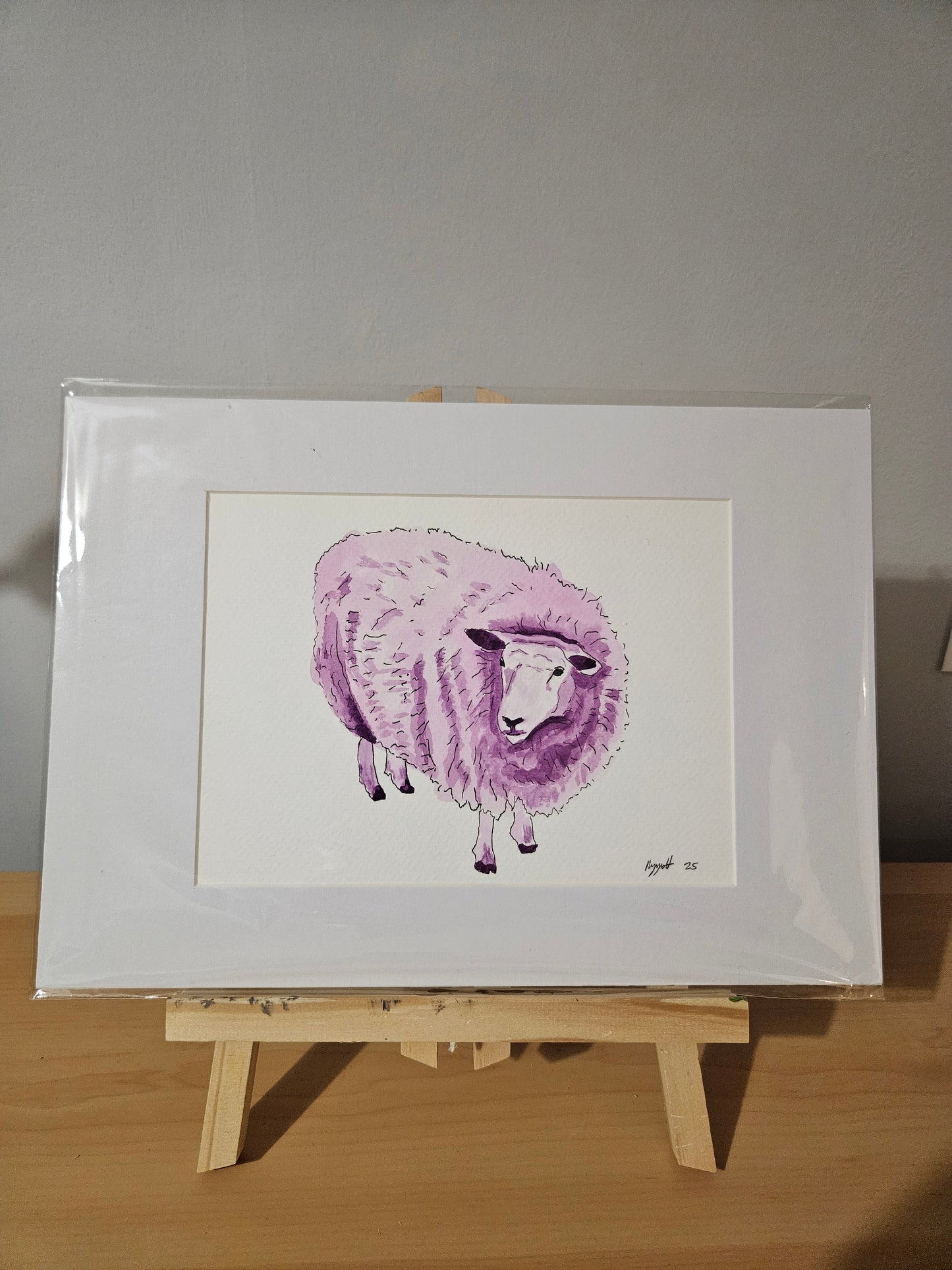 Watercolour painting of a purple sheep, mounted and displayed on an easel.