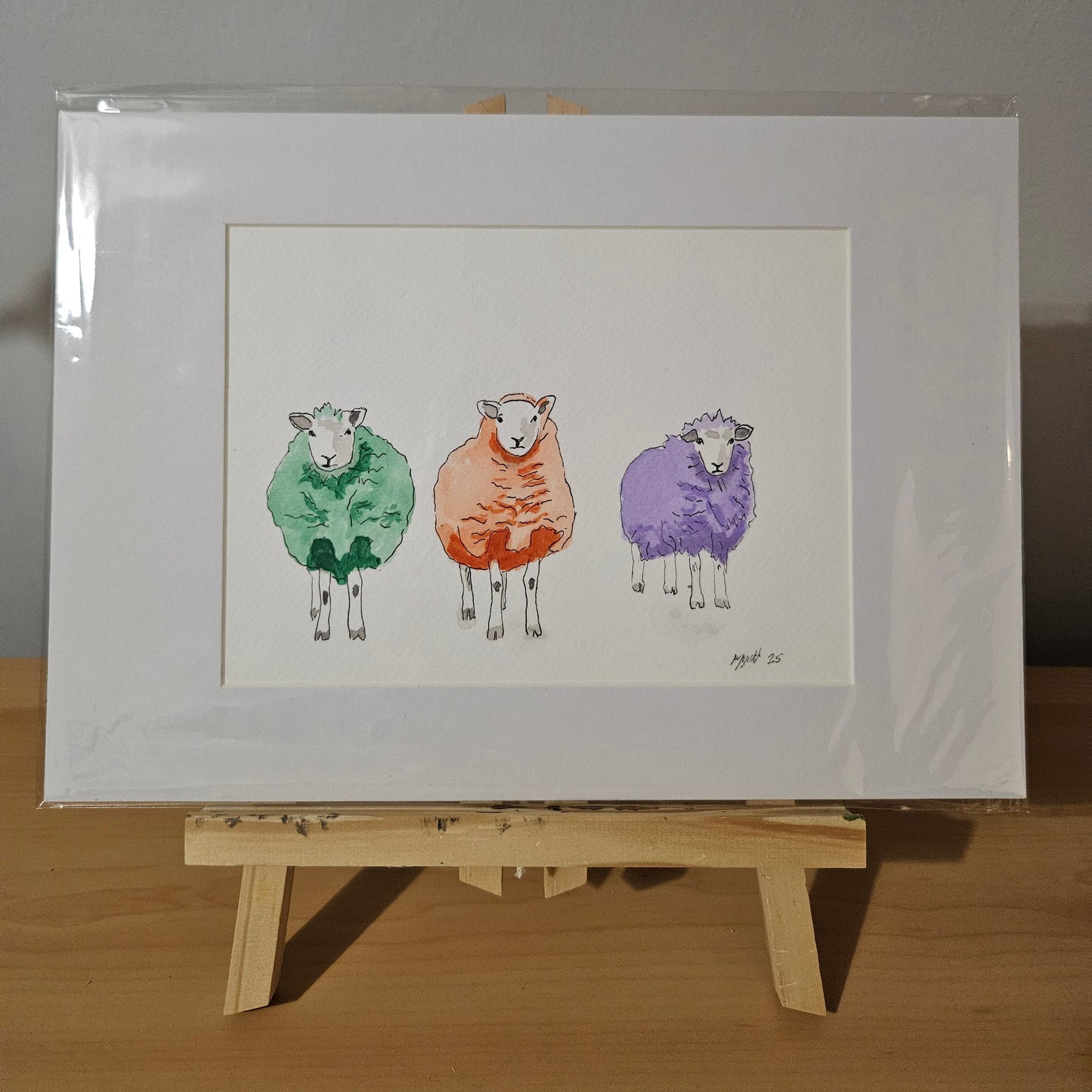 Mounted watercolour painting of three sheep, a green, orange and purple sheep.